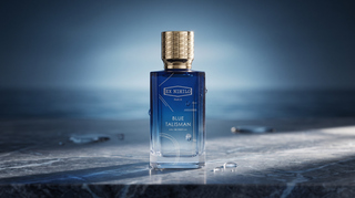 Ex Nihilo Blue Talisman perfume bottle on a dark marble surface with a blue ocean-toned background