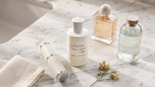 Five perfume bottles, including Juliette Has a Gun Not a Perfume, arranged on a marble vanity in soft daylight