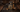 Initio Oud for Greatness bottle on dark charred wood surrounded by agarwood chips with incense smoke rising behind it